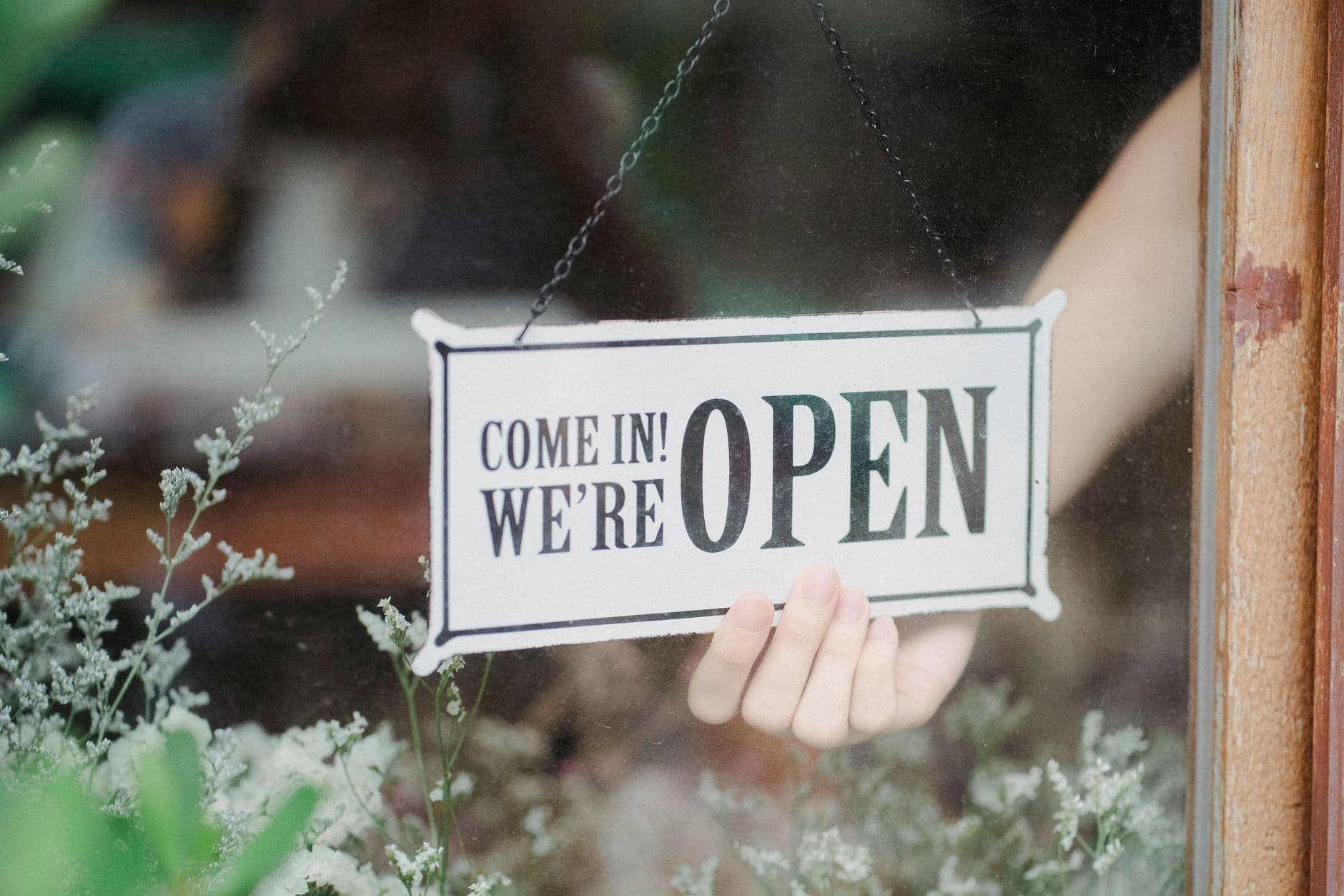 Çiçekçi vitrininde "Come in! We're open" tabelasını çeviren el